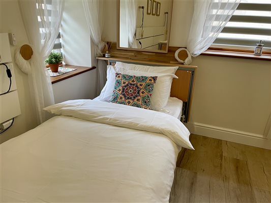 Profiling bed in the master bedroom, with white bed linen and green cushion.